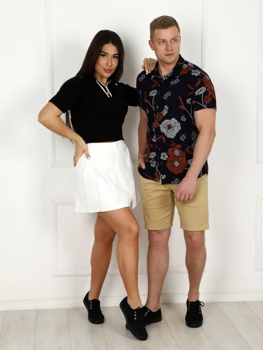 Two people standing against a white wall, wearing casual clothing.